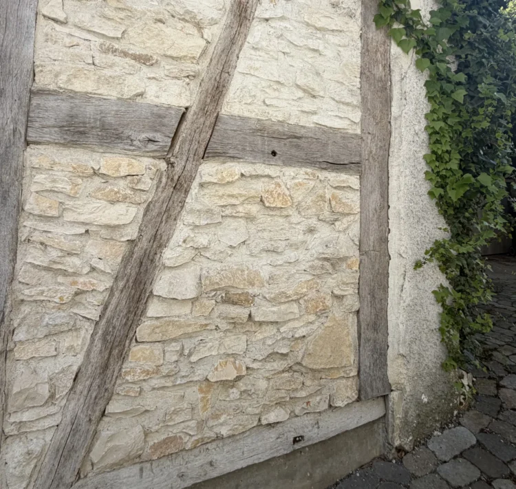 Verwittertes Fachwerk mit Holzbalken und Natursteinausfachung an einer Altbauwand