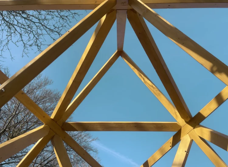 Detailaufnahme einer Holzdachkonstruktion von unten, Sparren treffen sich sternförmig vor blauem Himmel